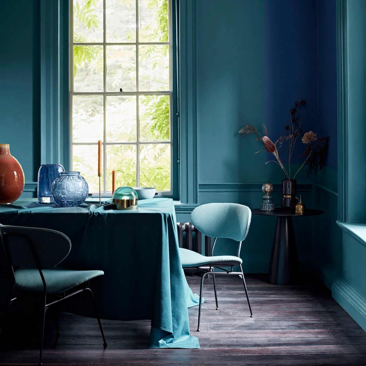 Teal dining corner with matching wall trim, a cloth-covered table and pale blue chairs near a window