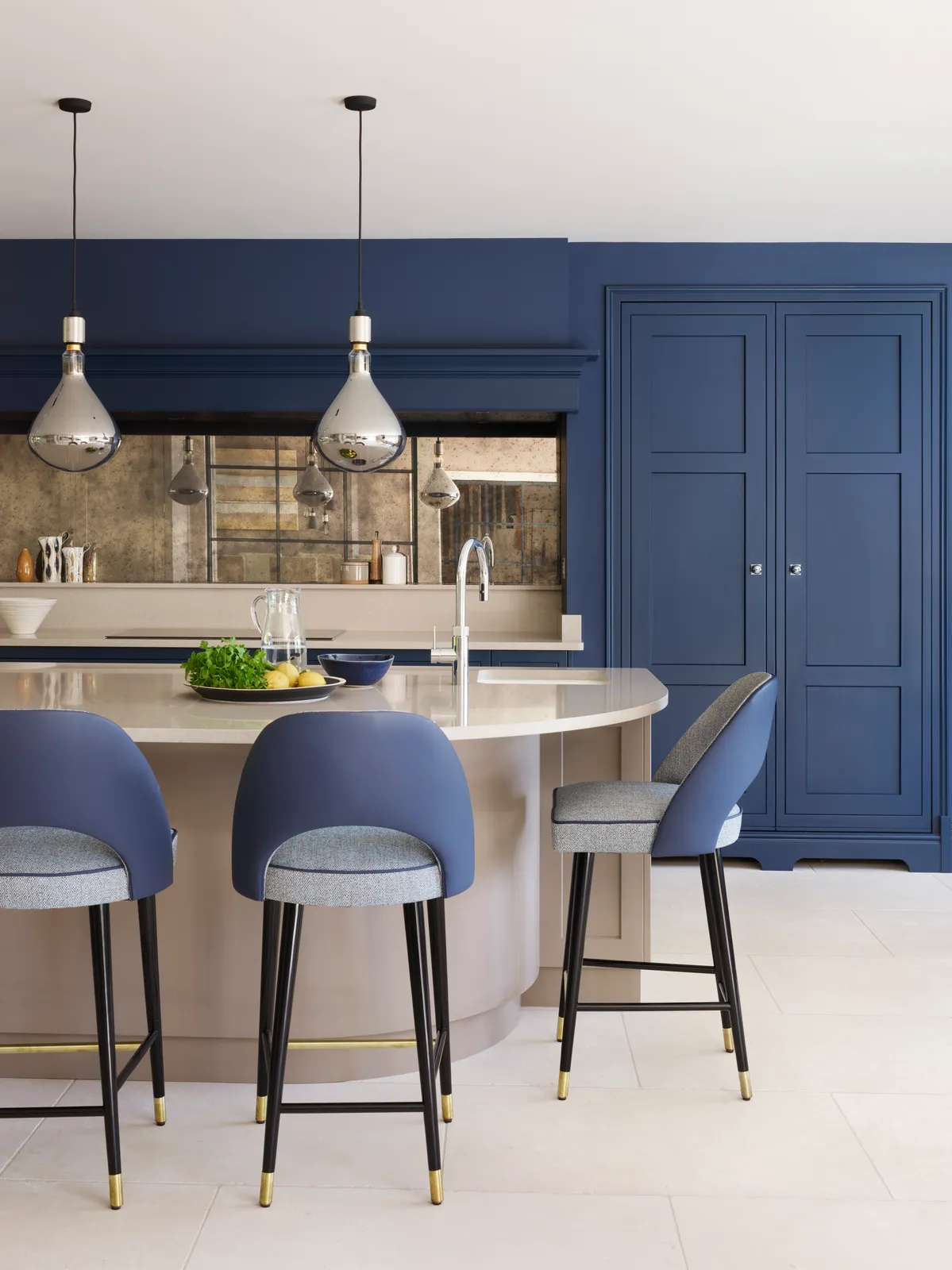 Deep blue full-height cabinets stand behind a pale island and blue upholstered stools