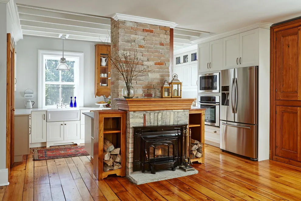 White kitchen cabinetry surrounds a timber-framed fireplace and warm wood floor