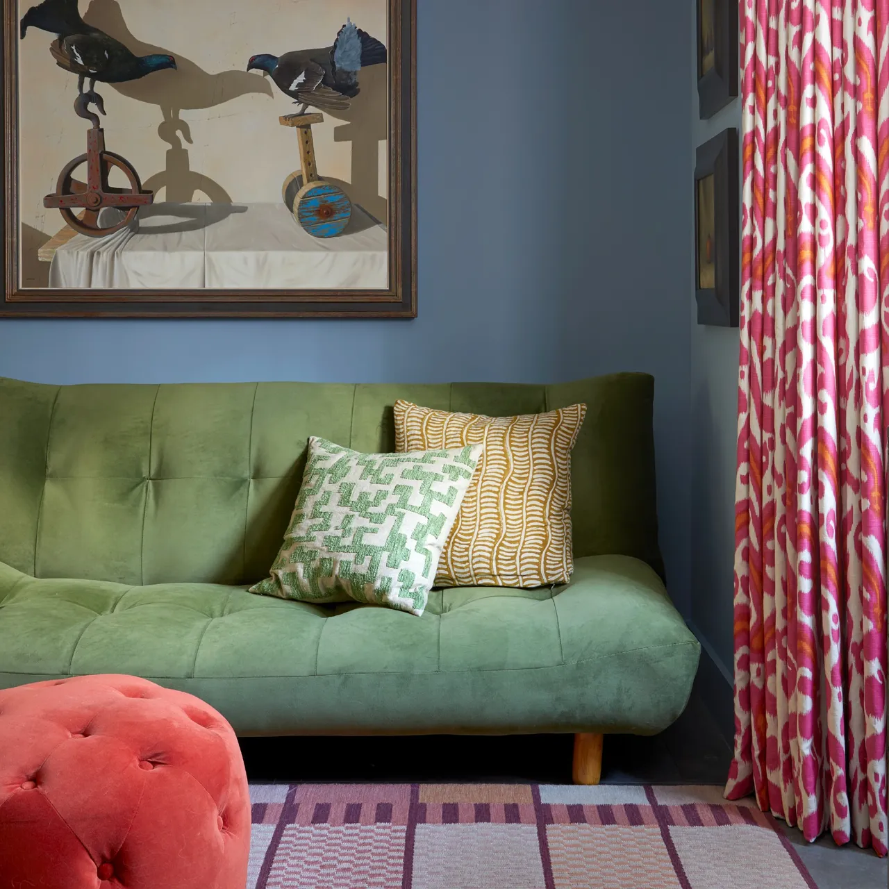 A compact green sofa sits beside a colorful curtain and a red footstool