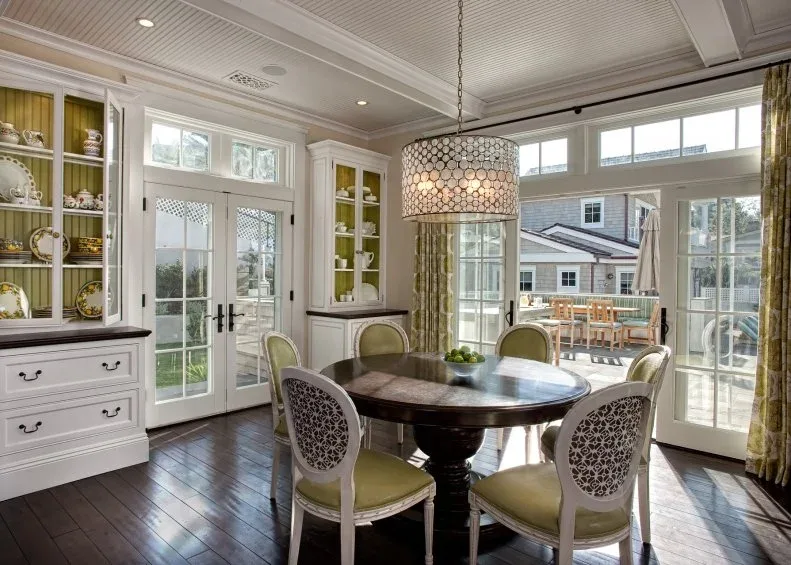Round dark table with pale decorative chairs beside a white display cabinet with yellow-backed shelves.