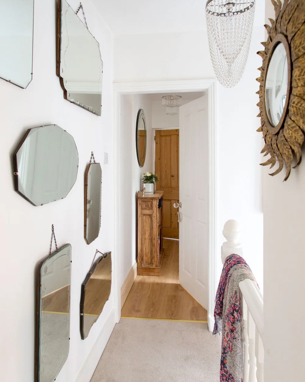 Pale hallway with a group of differently shaped mirrors, a sunburst mirror and a small wooden table near the front door.