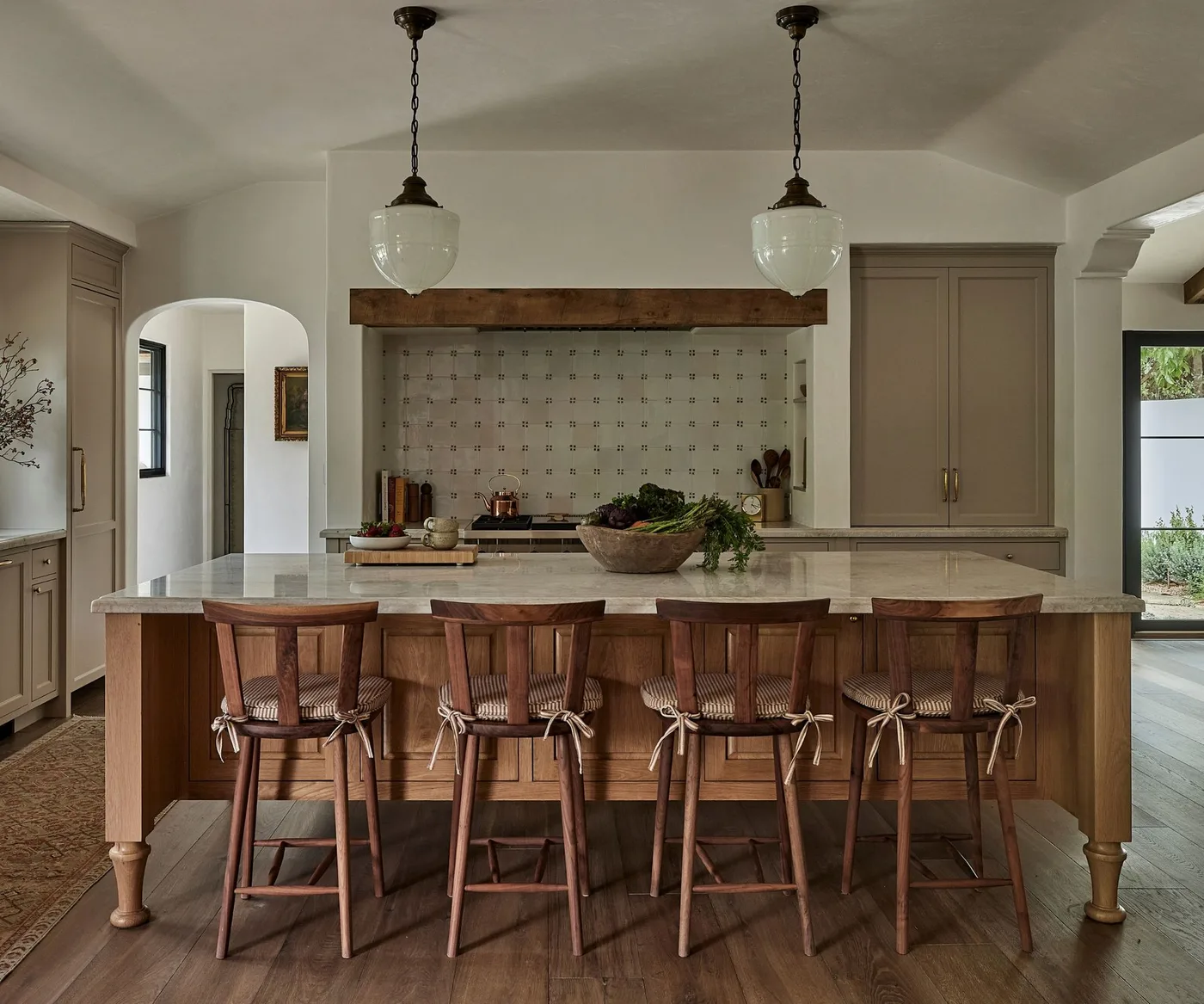Pale framed kitchen cabinets with small blue motifs on square backsplash tiles, a wooden hood edge and a wooden island.