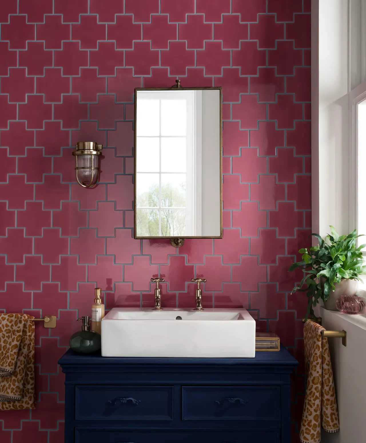 Pink geometric wall pattern above a dark blue vanity with a white vessel basin and brass-framed mirror