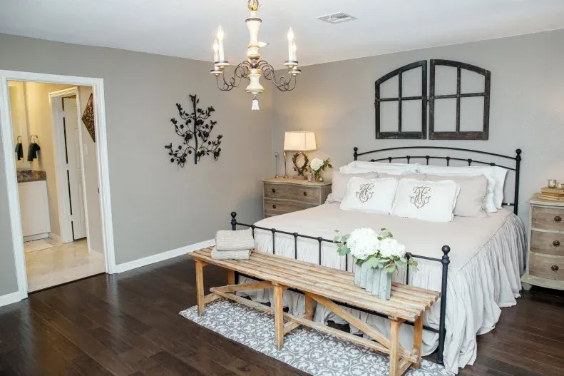 Pale wood slatted bench at the foot of a dark metal bed with neutral bedding and wood bedside chests