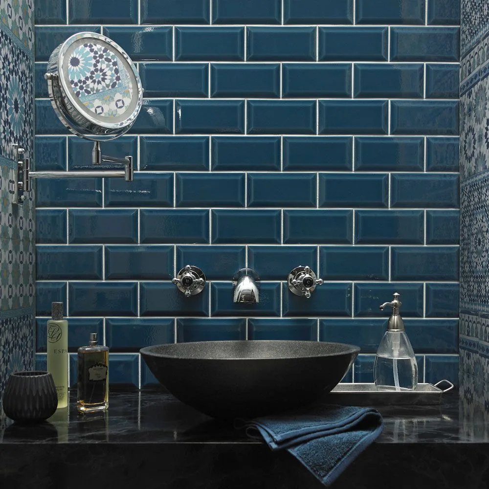 Glossy dark blue rectangular tiles sit behind a dark vessel sink beside patterned side walls