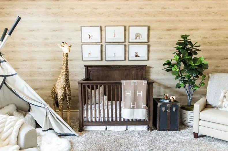 Dark wooden crib beneath animal-picture group against pale textured wall with decorative giraffe and lighter adult seating.