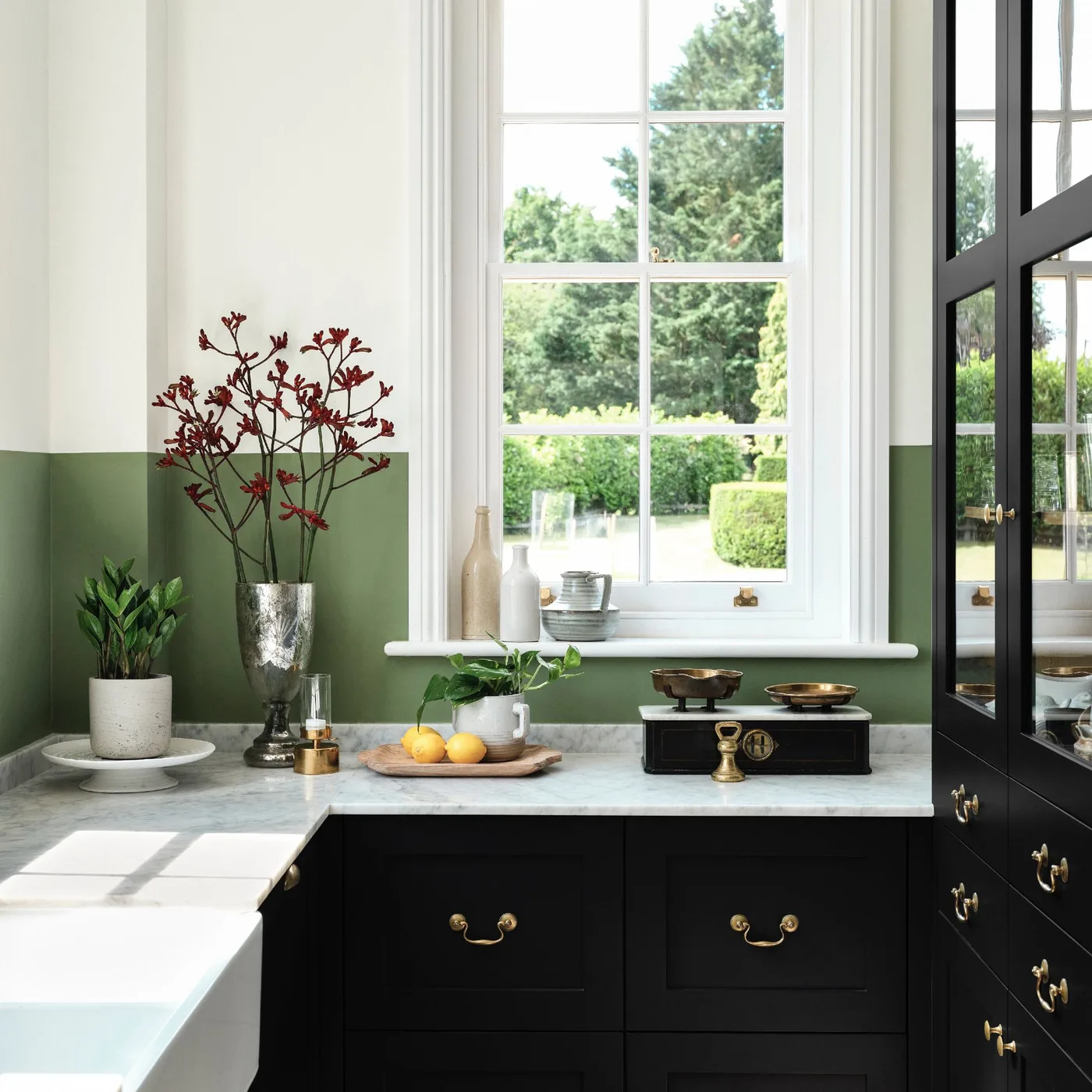 Compact kitchen with dark framed cabinets, pale worktops, a green painted wall section and a large window.