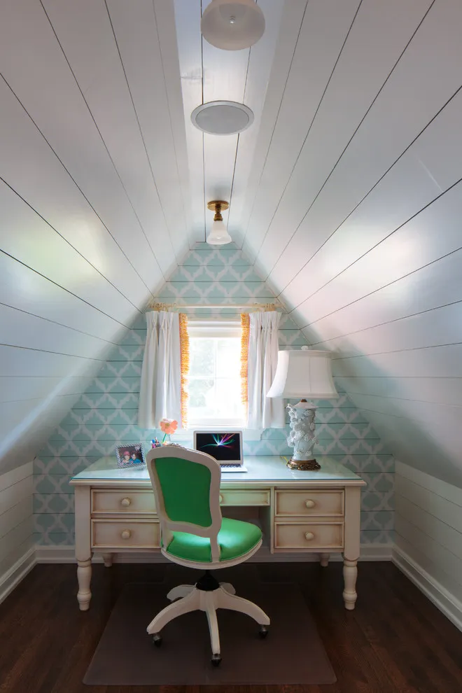 A small desk with a green chair sits beneath an attic window and pale paneled roof