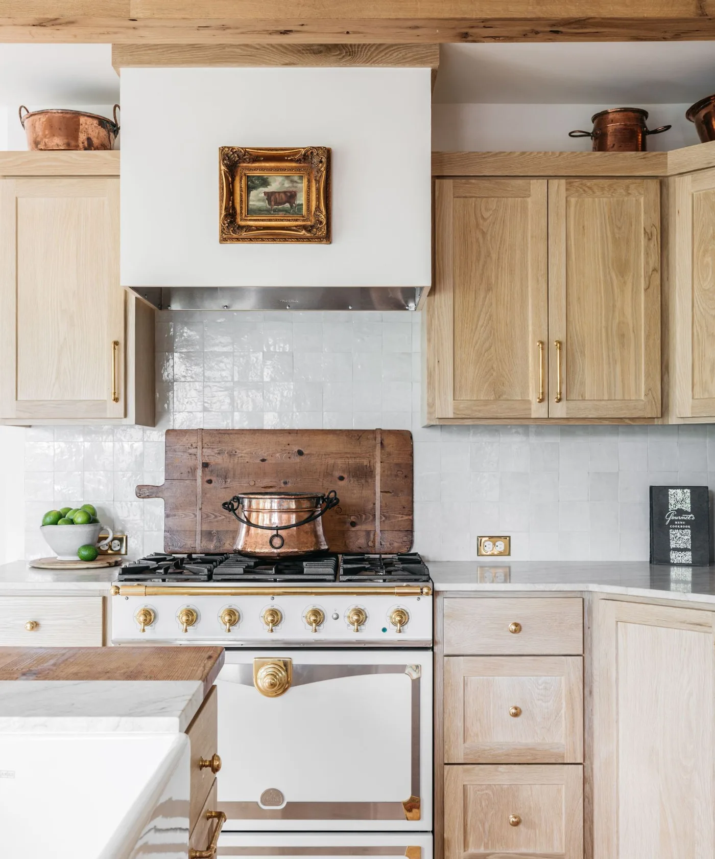 Kitchen with pale wooden cabinets, white hood, gray tile, cream cooker and warmer metal details.