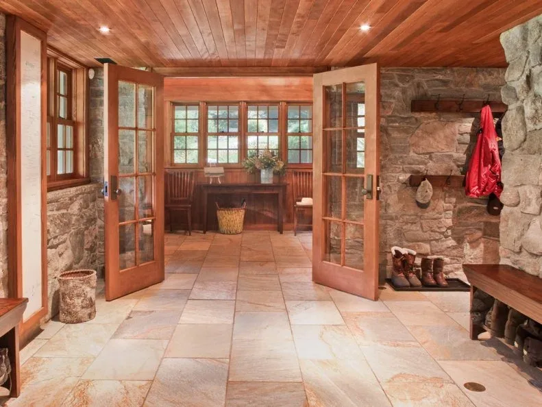 Country entrance hall with rough stone walls, wood ceiling, glazed wood double doors, coat hooks and wood bench