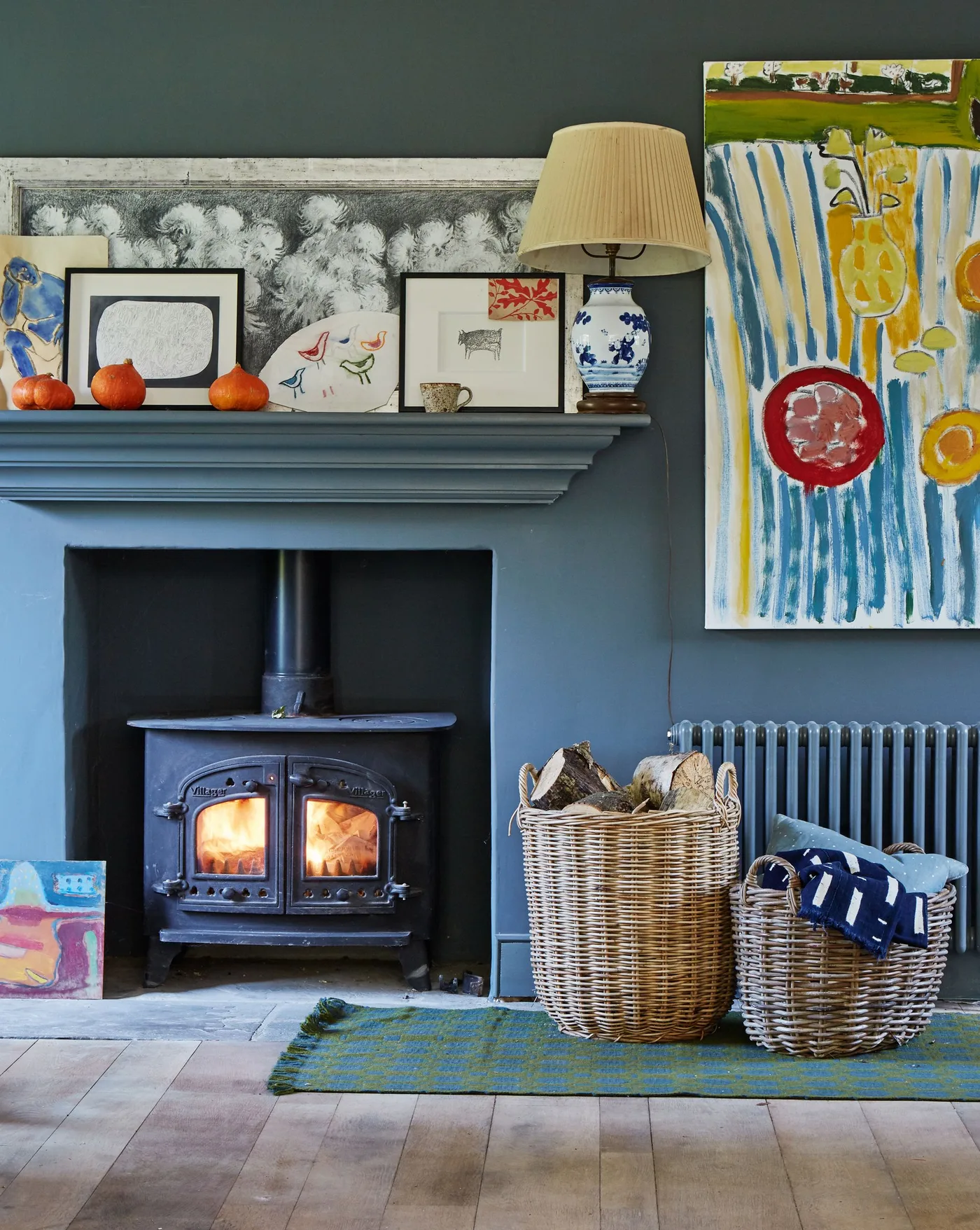 Dark teal fireplace with blue stove, two woven baskets, colorful artwork and a small green rug