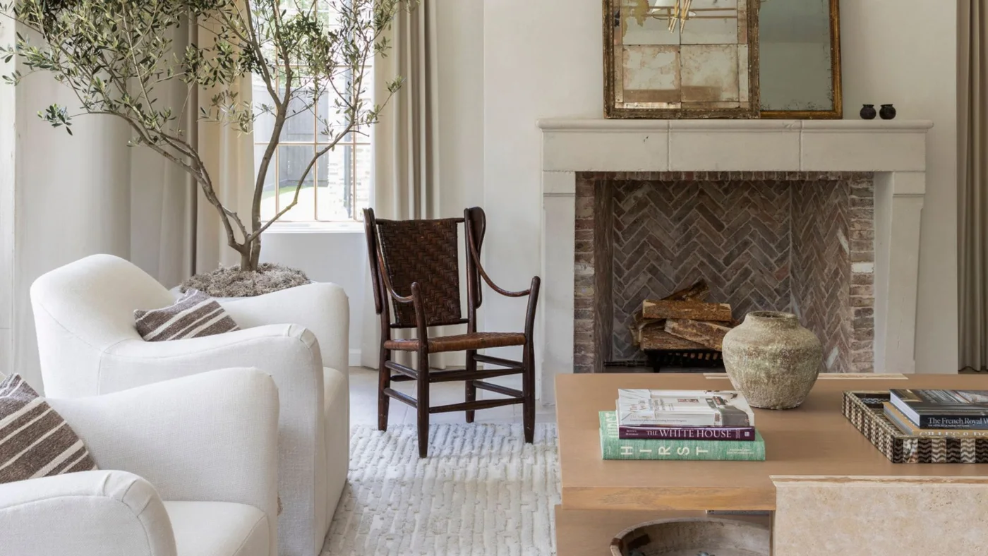 A pale mantel frames a herringbone-patterned brick firebox beneath a divided mirror beside white chairs and a wooden table