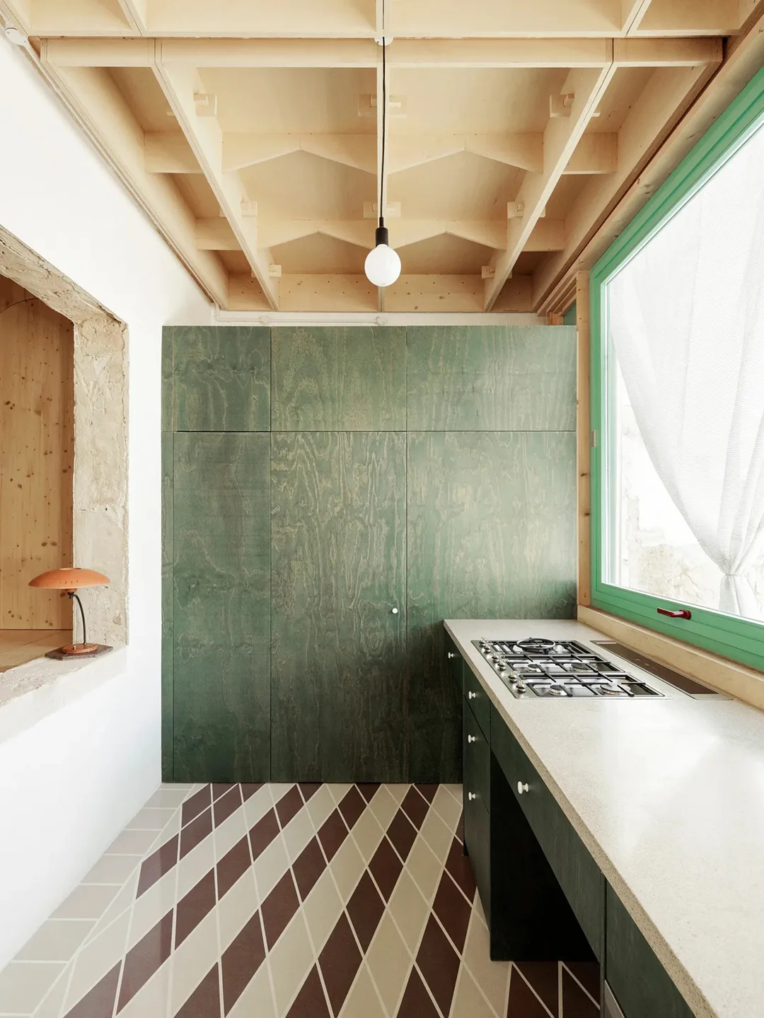 Green-grained tall cabinet doors stand beside a pale counter and cooking surface beneath a light wooden ceiling