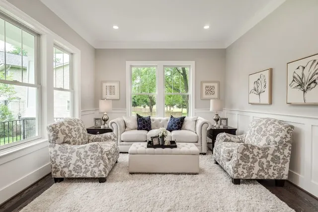 Two patterned chairs sit beside a pale sofa in a bright room with broad windows.