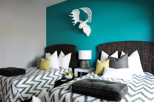 Two dark woven headboards sit against a strong teal wall with patterned bedding below.