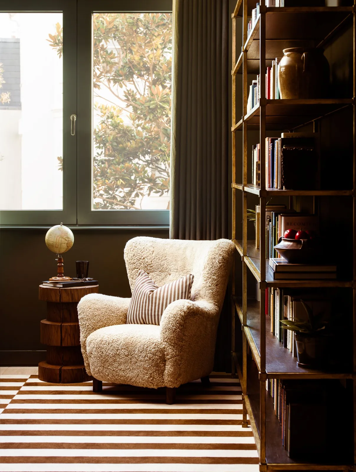A textured pale chair sits beside tall bookshelves on a striped rug.