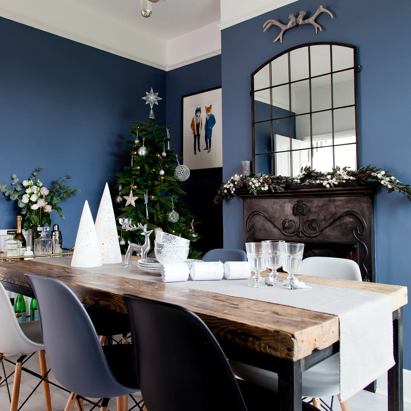 Dark arched grid mirror above an ornate fireplace in a blue dining room dressed with seasonal greenery