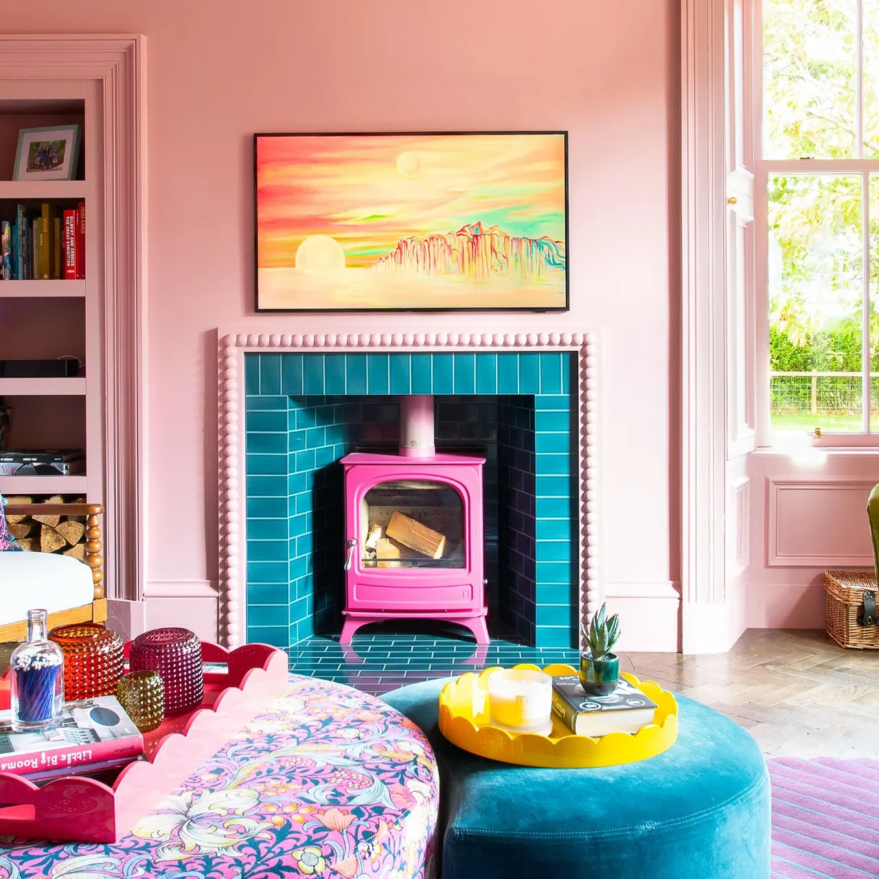Pink room with turquoise-tiled fireplace, bright pink stove, colorful picture and rounded footstools