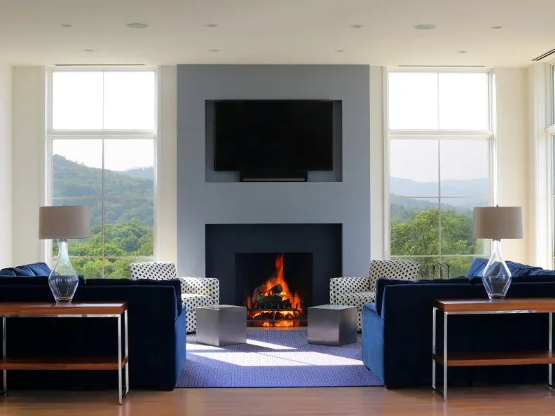 Smooth gray fireplace wall with television centered between tall windows and navy sofas