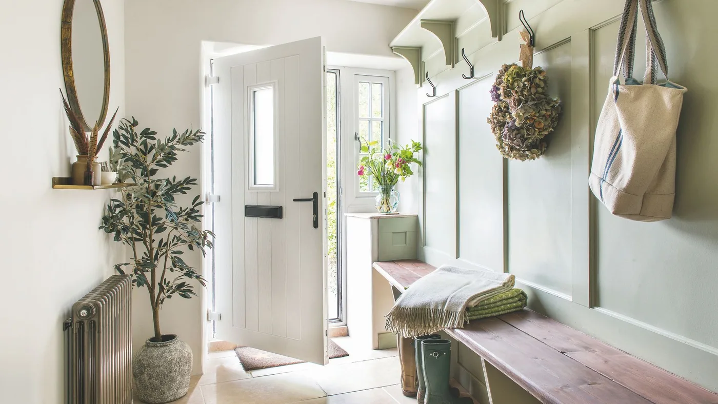 Pale green paneled entry with long wood bench, lower cubbies and boots, upper shelf and hooks beside open white door