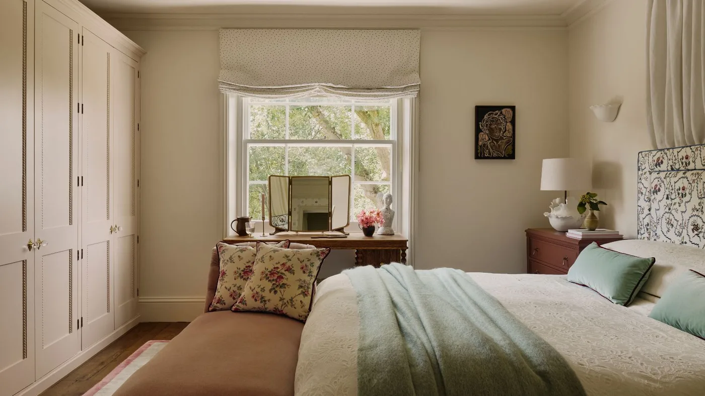 Cream bedroom with fitted paneled wardrobes, a patterned headboard, dressing table and upholstered bench.