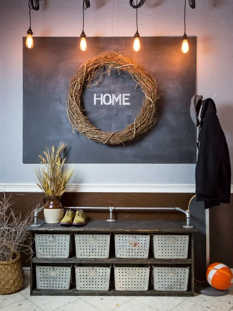 Rustic shoe storage unit with eight pale perforated baskets, pipe-style rail, twig wreath and exposed hanging bulbs against gray wall