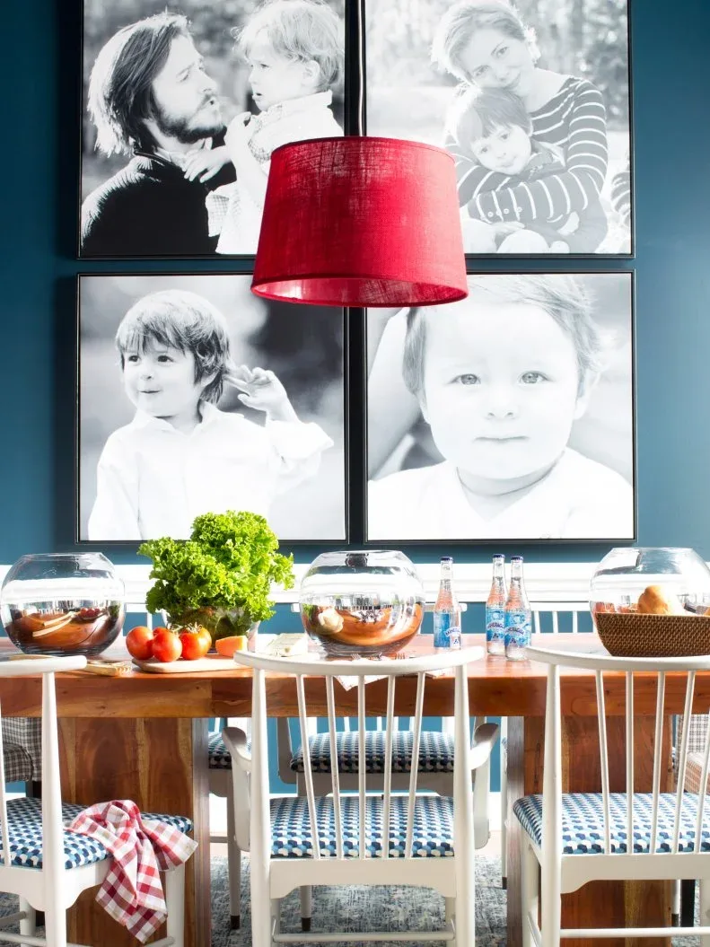 Four large black-and-white family photographs in black frames on a blue dining-room wall, above a wooden table and white chairs with patterned seats.