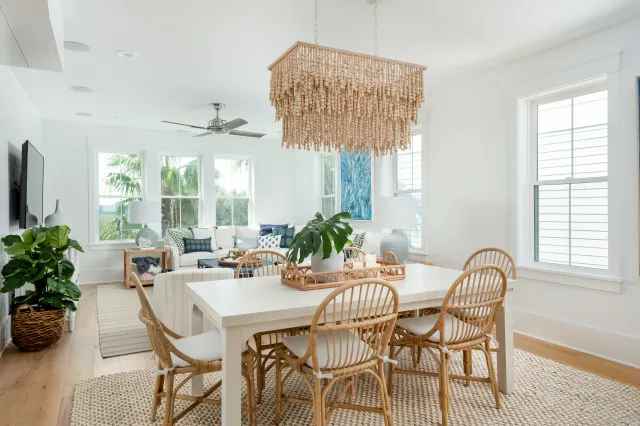 Cane dining chairs around a pale table beneath a large fringed beaded pendant