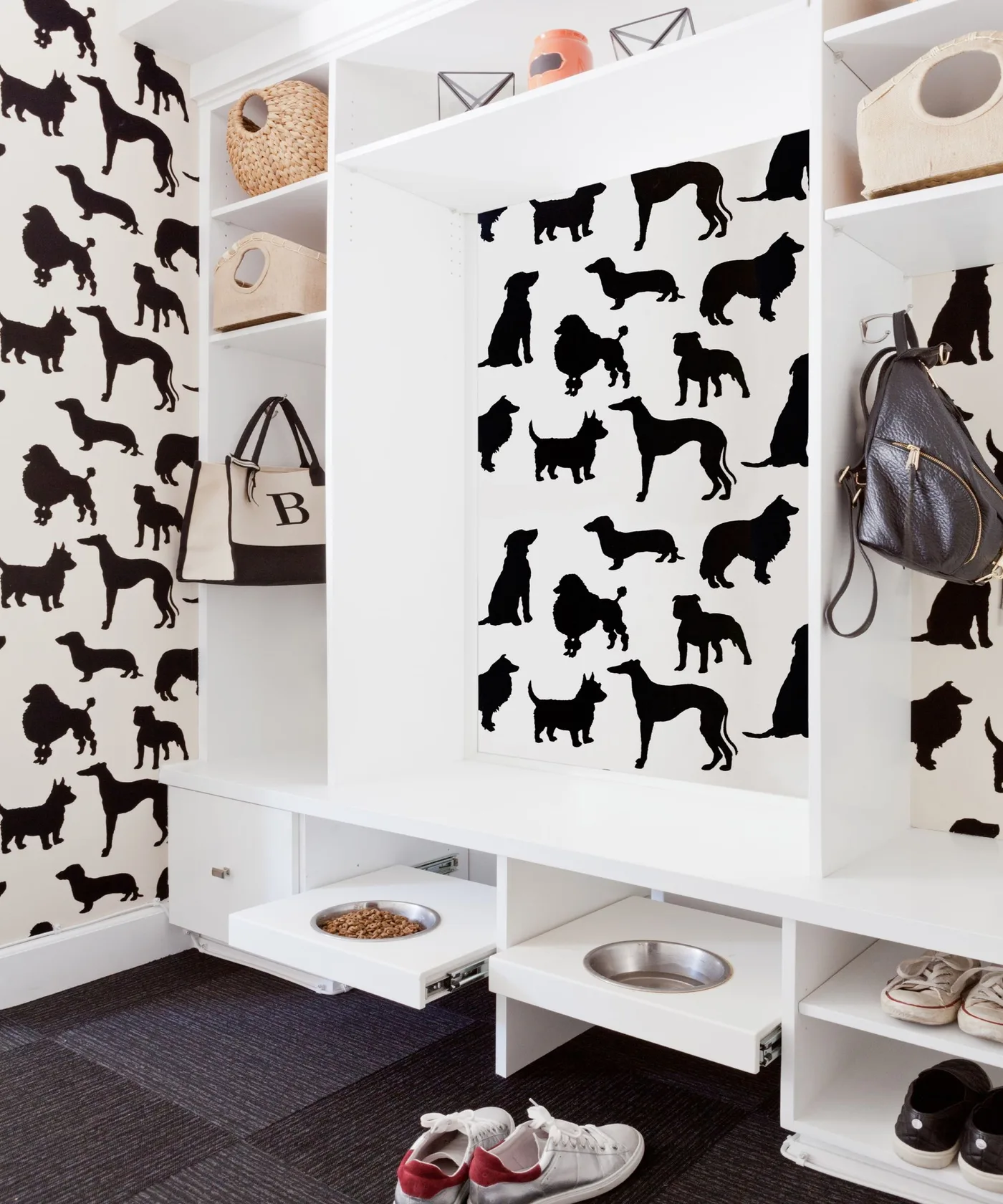 White mudroom with black dog-pattern wallpaper, open baskets, coat hooks, shoe shelves and pull-out pet bowl trays