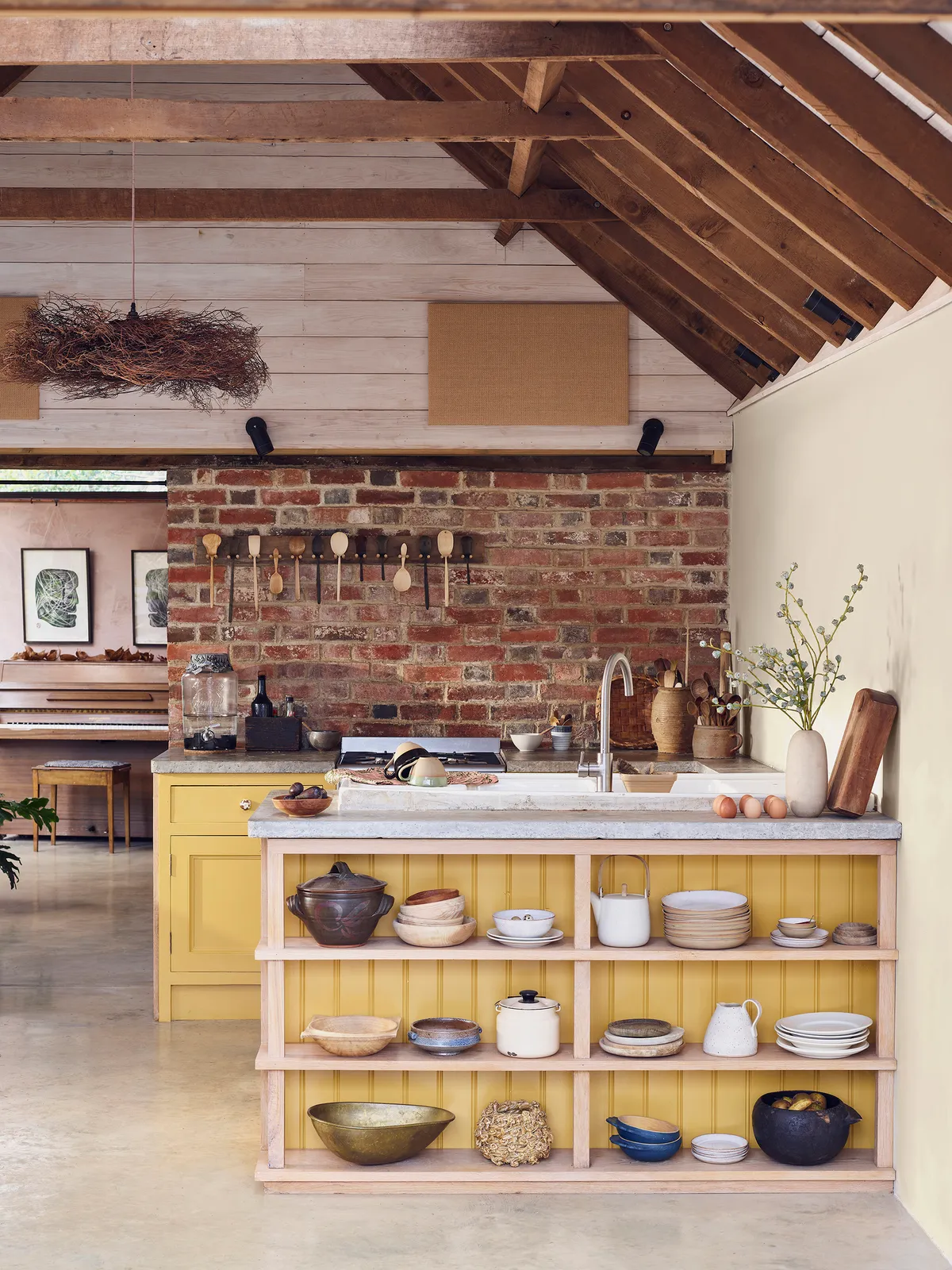 Yellow kitchen cabinets and open shelves below a pale counter with exposed brick and timber beams