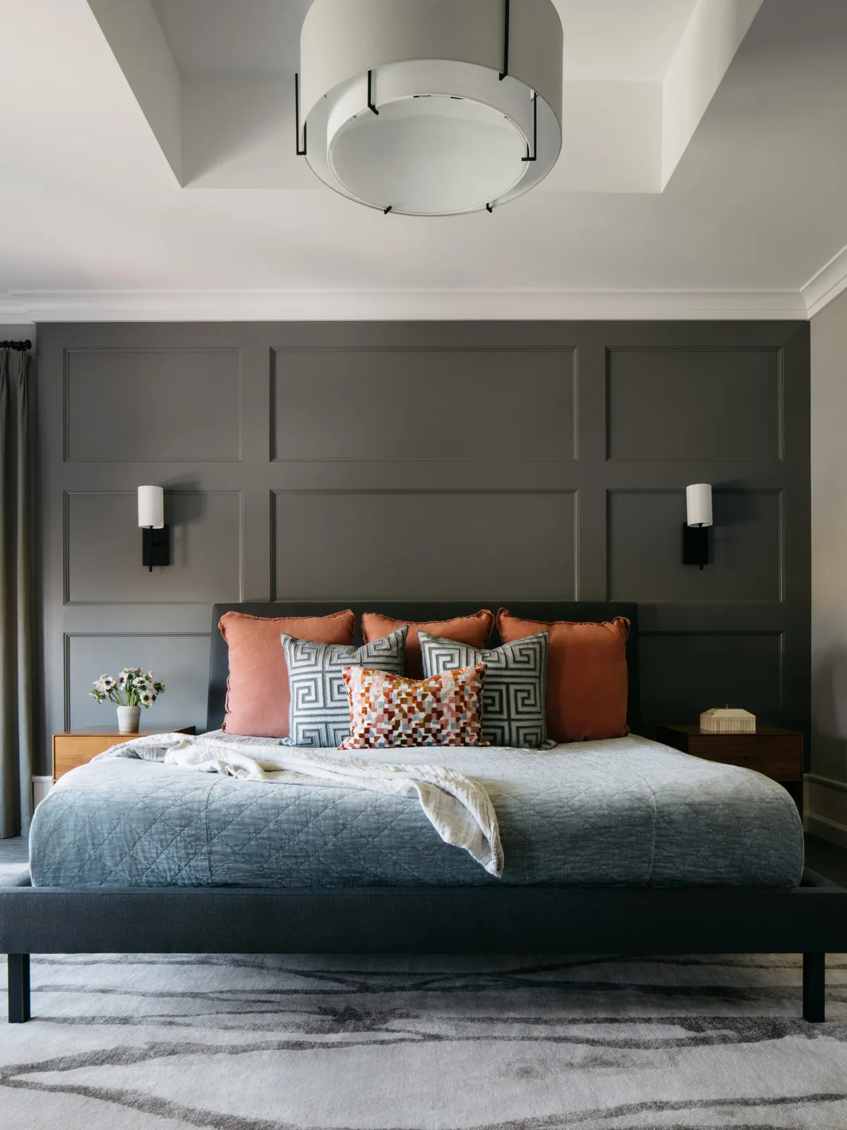 Charcoal wall paneling frames a dark bed topped with warm-colored pillows.