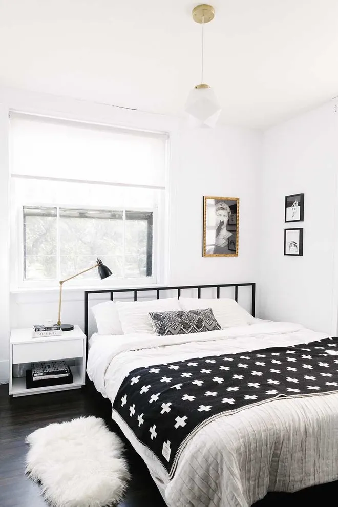 A black patterned cover sits on a white bed below a slim black metal frame