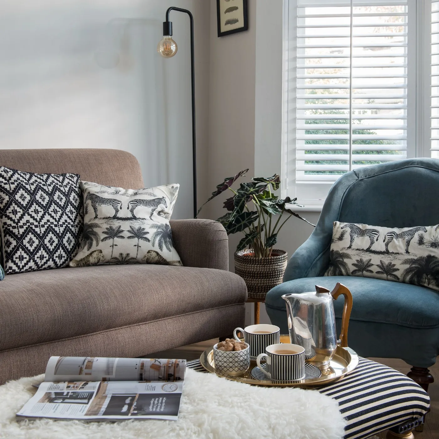Taupe couch with black-and-white geometric and animal-print pillows beside a blue chair carrying a matching animal print.