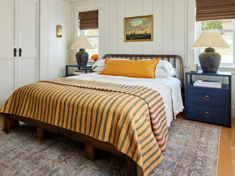 White paneled bedroom with wood bed, mustard striped blanket and dark blue bedside chests