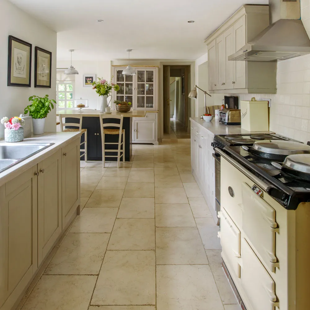 Cream paneled cabinets and pale floor tiles lead toward a dining area with a glazed dresser