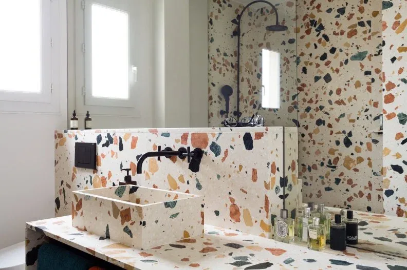 Pale bathroom surfaces with rust, green and dark flecks around a square vessel basin and black fittings