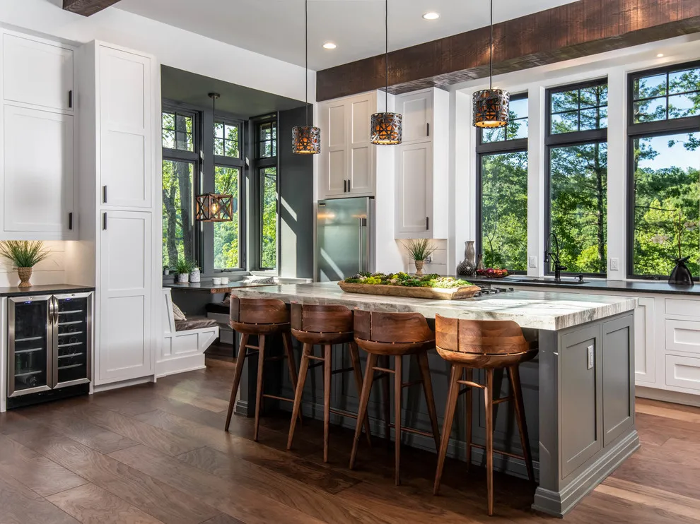 A taupe island sits beneath a dark timber beam beside large black-framed windows