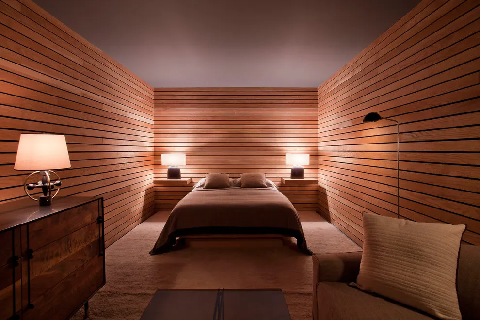 Horizontal timber boards wrap a narrow bedroom around a bed with brown bedding