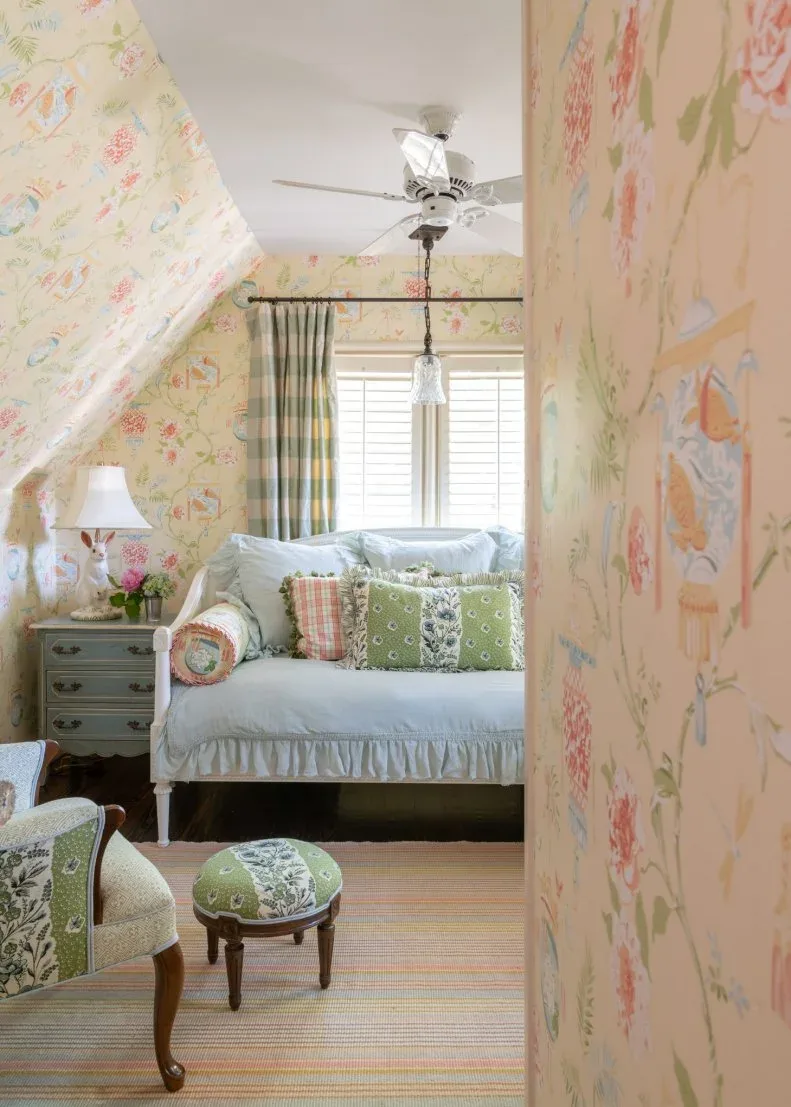 Small sloped-ceiling bedroom with pale yellow floral wallpaper, pale blue daybed and green patterned cushions