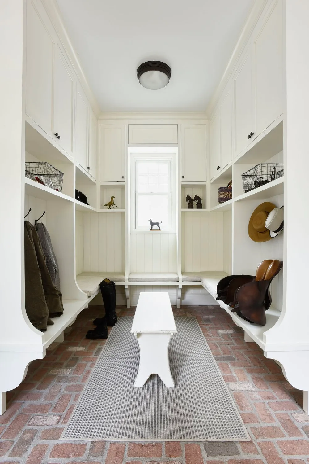 White storage benches along both sides of a mudroom with brick-toned flooring and a narrow central bench.
