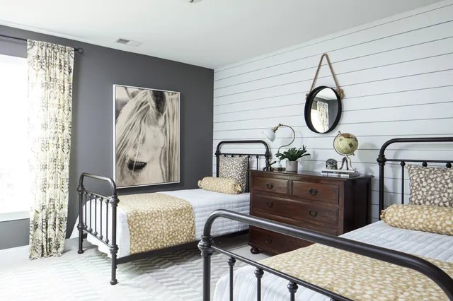 Two dark metal beds flank a timber nightstand against pale horizontal paneling.