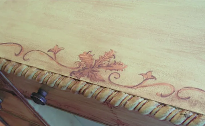Close view of a pale green desktop with reddish leaf decoration and a warm carved edge.