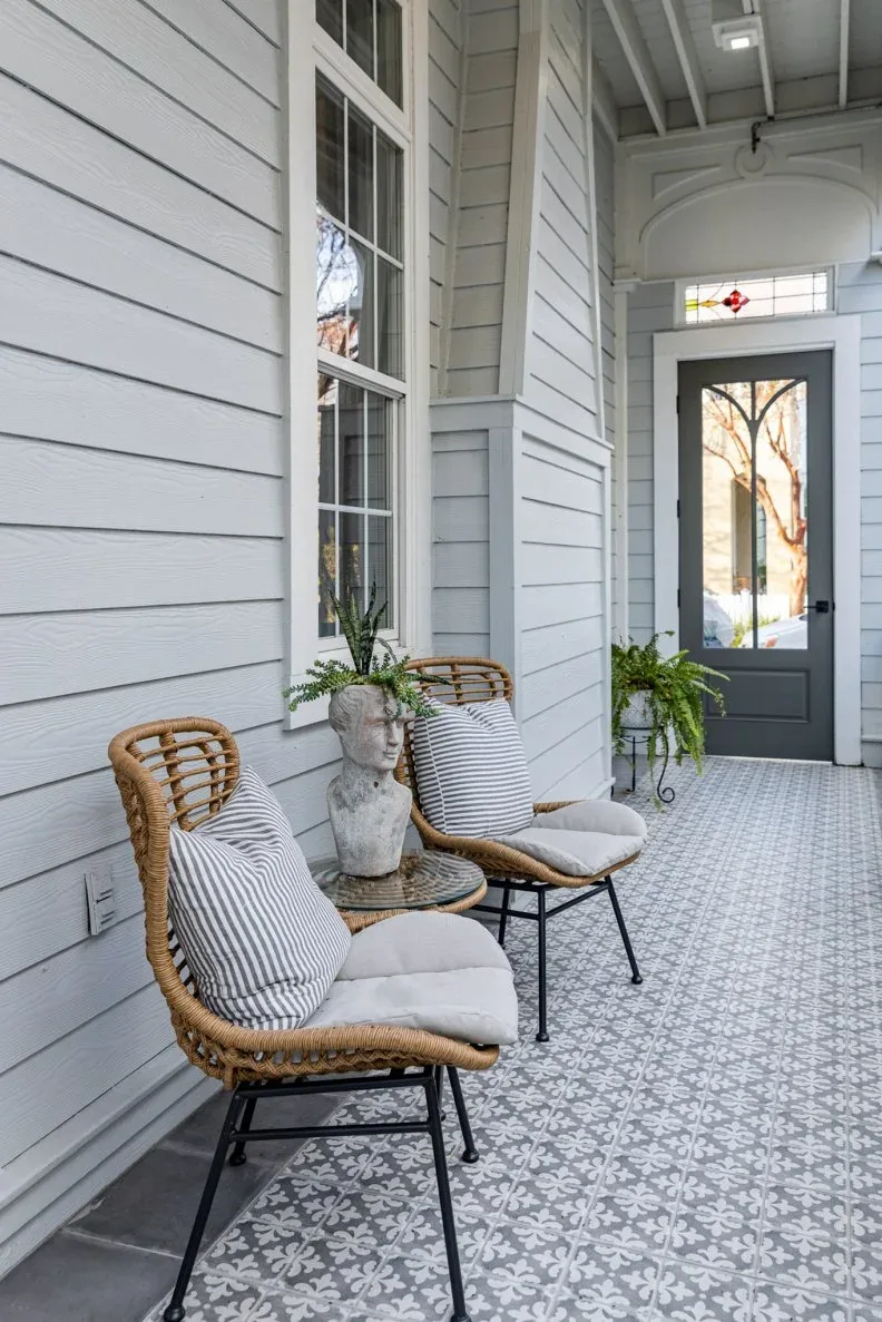 Pale gray porch with two woven chairs, striped cushions and gray patterned tile-looking floor