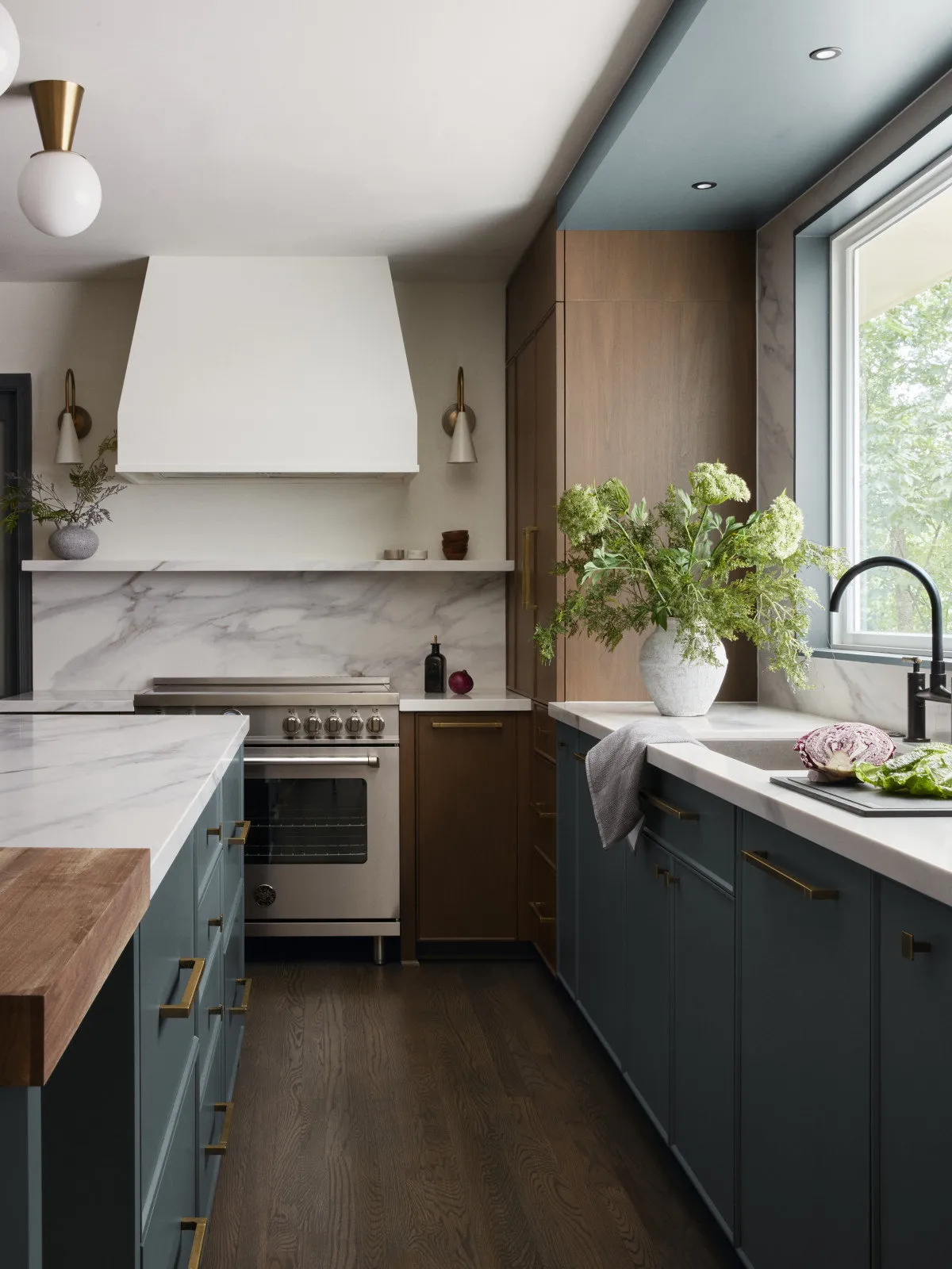 Dark lower cabinets face a wide window in a kitchen with timber upper storage.