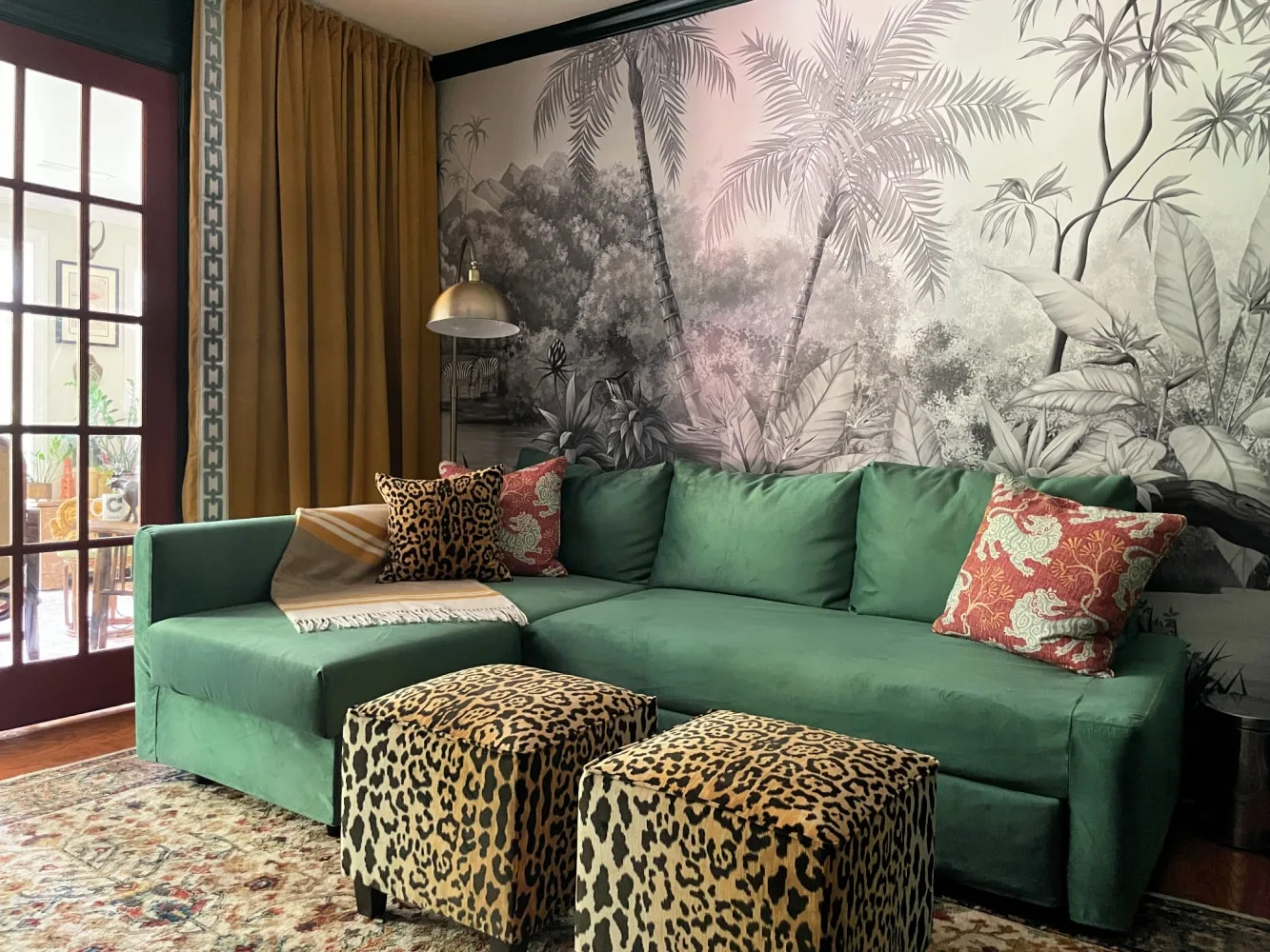 Green office sofa beneath a gold-toned hanging lamp with mustard curtains and patterned stools.