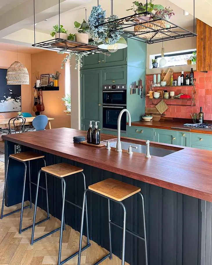 Dark painted kitchen island with thick timber worktop, stools and overhead suspended plant racks