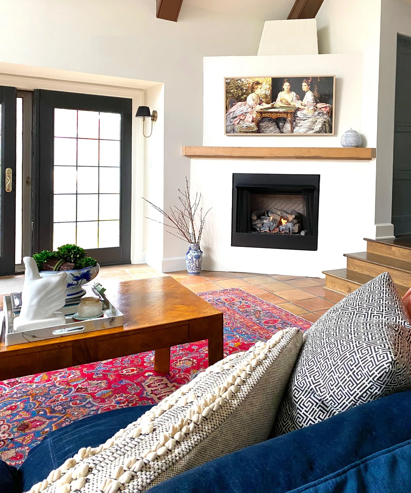 White angled fireplace with a wood mantel, framed painting and blue sofa in front.