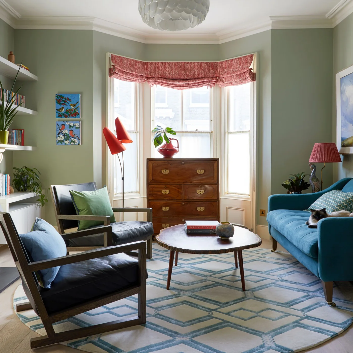A blue sofa and two dark wooden-framed chairs sit on a geometric rug in a pale green room