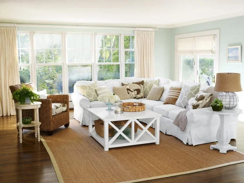 Soft green living room with a white sectional, patterned green cushions, white table and woven chair.